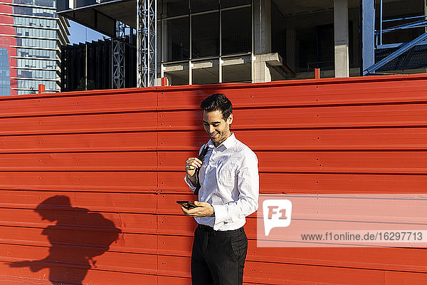Male entrepreneur using mobile phone while standing against red wall in city
