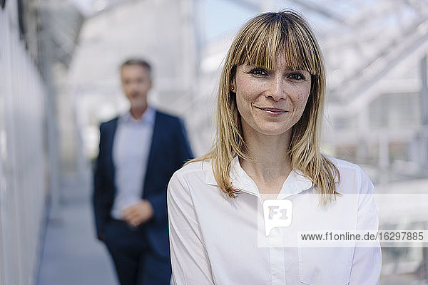 Nahaufnahme einer lächelnden Geschäftsfrau mit einem männlichen Mitarbeiter im Hintergrund im Gewächshaus