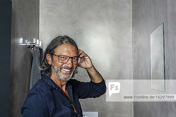 Cheerful man with hand in hair standing in bathroom