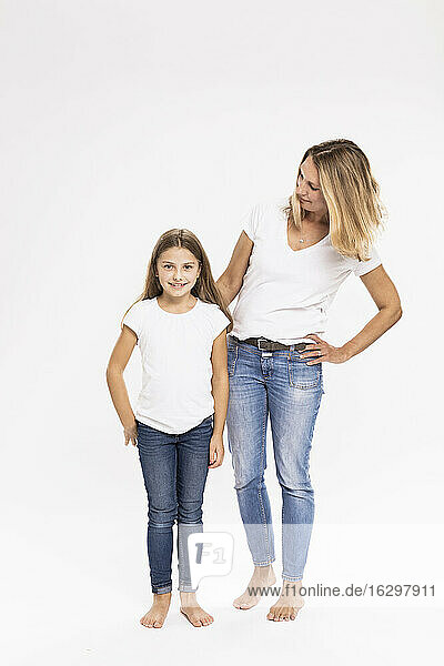 Mother with hand on hip looking at daughter while standing against white background