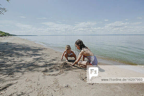 Schwestern spielen im Sand im Sommer am Strand an einem sonnigen Tag