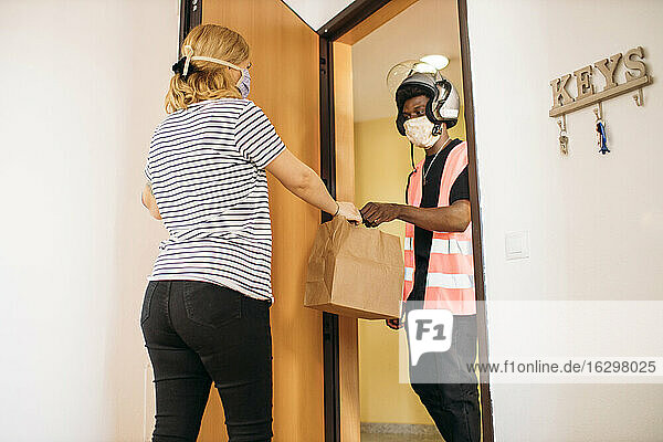 Frau nimmt Papiertüte von Liefermann mit Schutzmaske