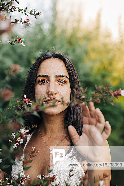 Junge Frau steht an einer blühenden Pflanze in einem öffentlichen Park