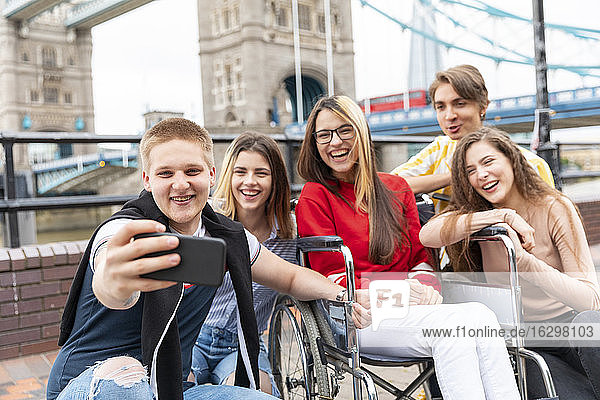 Happy young male and female friends taking selfie with Tower Bridge in background  London  UK