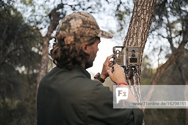 Älterer männlicher Fotograf  der eine Überwachungskamera auf einem Baumstamm im Wald positioniert
