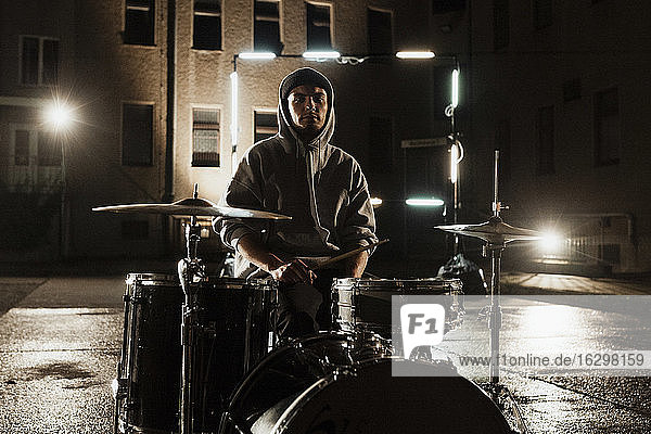 Young male drummer sitting with kit at back yard during night