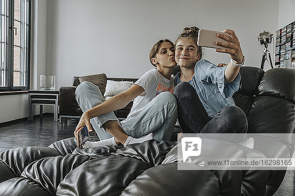 Friends taking selfie with smart phone while sitting on couch at home