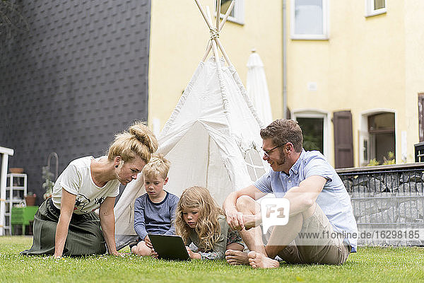 Family enjoying weekend at back yard with girl using digital tablet