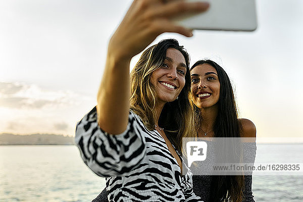 Freunde lächelnd während der Aufnahme selfie gegen klaren Himmel
