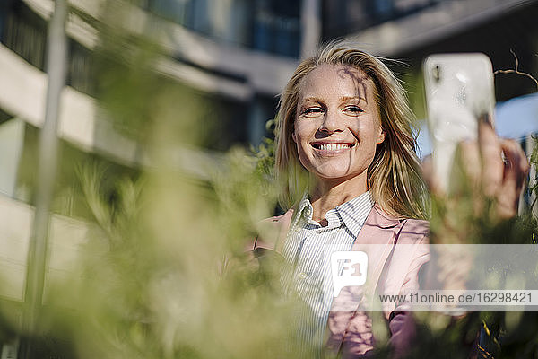 Smiling beautiful female entrepreneur taking selfie on sunny day