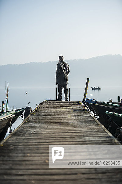 Mann steht auf einer Holzpromenade und schaut auf den See