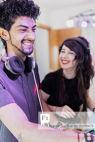 Fröhlicher junger Musiker mit weiblichem DJ  der sich beim Abmischen von Ton im Aufnahmestudio amüsiert