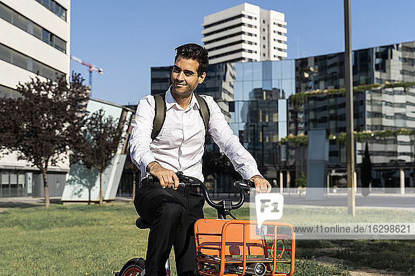 Male commuter riding electric bicycle against buildings in city