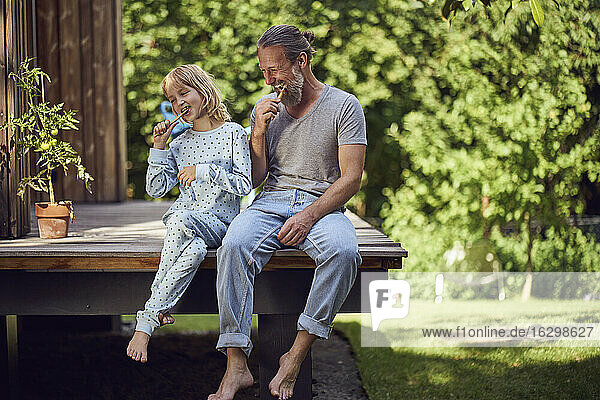 Vater und Tochter beim Zähneputzen im Garten sitzend