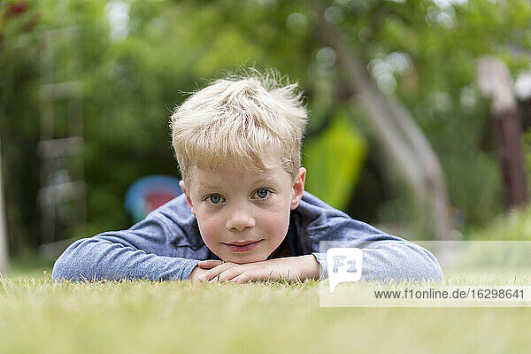 Niedlicher blonder Junge liegt auf Gras im Hinterhof