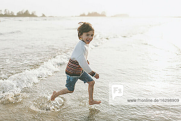 Cheerful boy running in water at beach