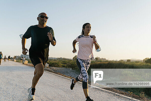 Woman running with senior sportsman on road during sunset