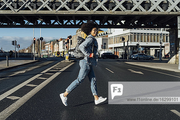 Unbeschwerte junge Frau mit Afro-Haar läuft auf der Straße in der Stadt während des sonnigen Tages