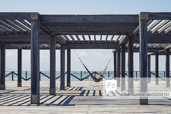 Frau in Hängematte liegend  die an einer Metallstruktur auf der Promenade hängt  an einem sonnigen Tag