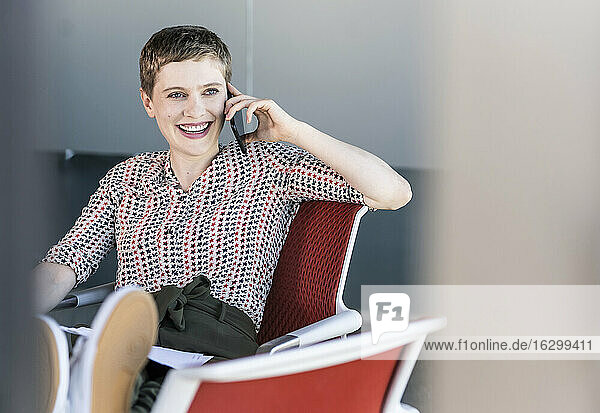 Glückliche Geschäftsfrau  die auf einem Bürostuhl sitzt und telefoniert