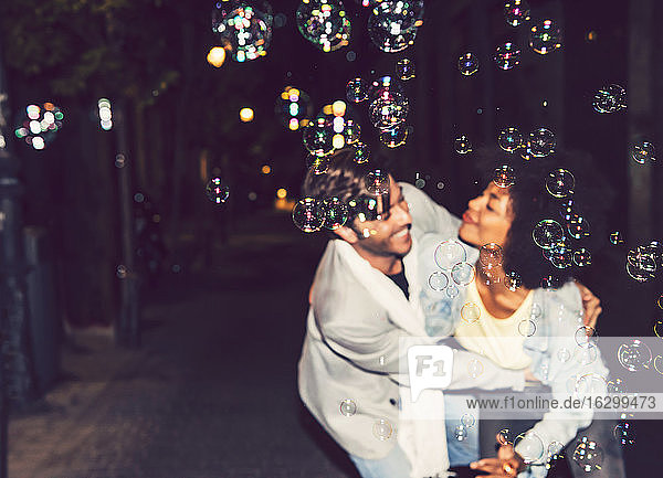 Nahaufnahme von Seifenblasen mit tanzendem Paar auf der Straße im Hintergrund bei Nacht