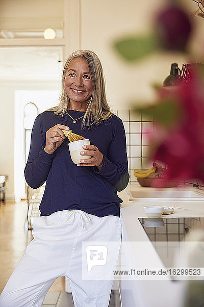 Lächelnde Frau beim Teemischen am Küchentisch