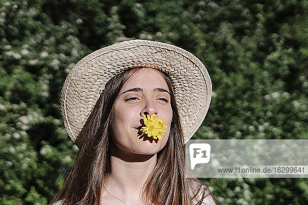 Junge Frau mit Hut und gelber Blume im Mund in einem Park im Frühling