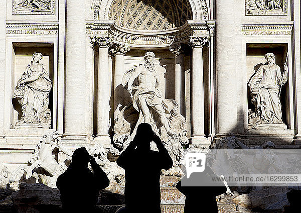 Italien  Rom  Blick auf den Trevi-Brunnen mit Silhouetten von drei Touristen davor