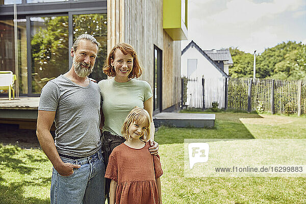 Lächelnde Familie steht vor einem kleinen Haus im Hof