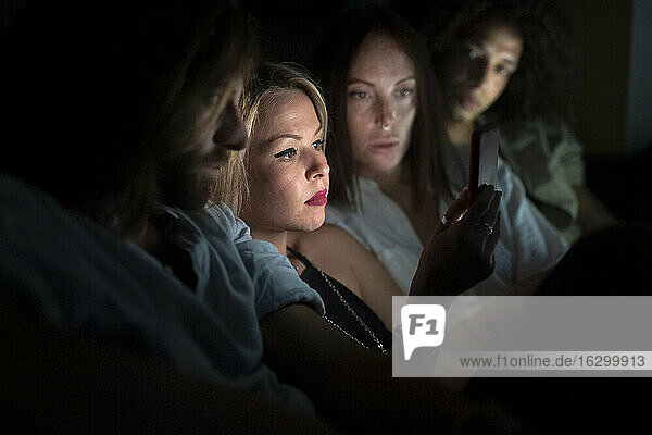 Männliche und weibliche Freunde schauen in der Nacht auf ihr Smartphone