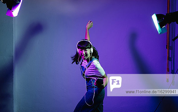 Fröhliche Frau  die singt und tanzt  während sie Musik über Kopfhörer vor einem Hintergrund hört