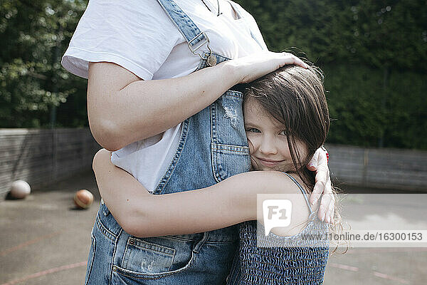 Daughter and mother embracing each other at back yard