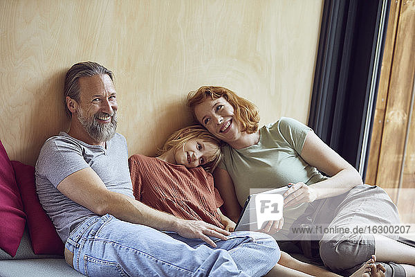Lächelnde Eltern mit Tochter  die ein digitales Tablet benutzt  während sie zu Hause auf dem Bett liegt