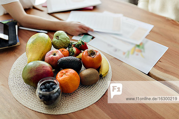 Frauenhand ordnet Papiere nach Früchten auf dem Tisch zu Hause