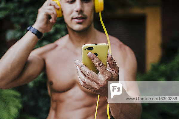 Close-up of shirtless man listening music through headphones while standing in yard