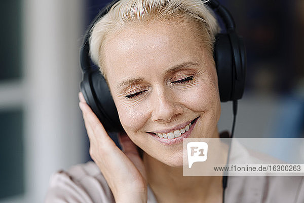 Nahaufnahme einer Geschäftsfrau mit geschlossenen Augen  die über Kopfhörer im Büro Musik hört