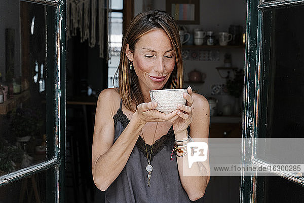Smiling woman with eyes closed holding bowl of matcha tea at cafe