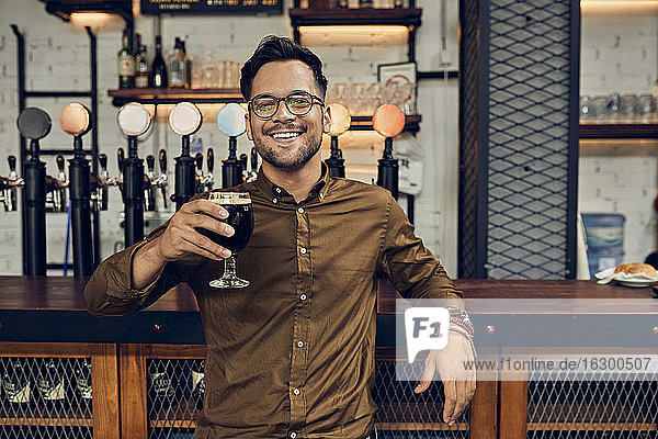 Porträt eines lächelnden Mannes  der sein Bierglas in einer Kneipe hebt