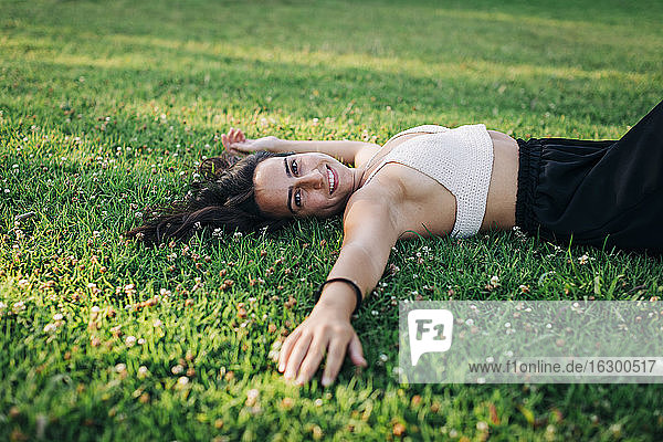 Lächelnde junge Frau entspannt sich im Gras eines öffentlichen Parks