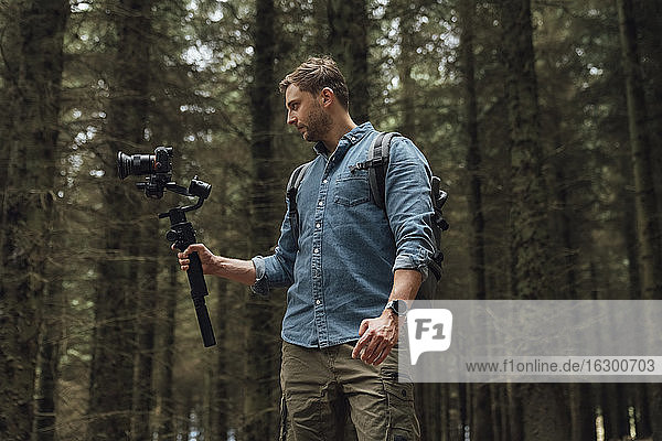 Man filming with camera and gimbal while standing against trees in forest