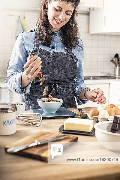 Lächelnde Frau wiegt Mandeln auf einer Küchenwaage zu Hause