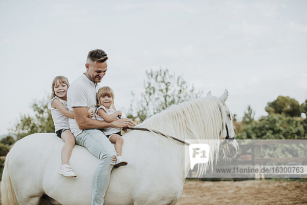 Vater mit Töchtern reitet Pferd in Scheune gegen Himmel