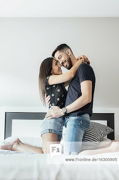 Smiling couple embracing each other on bed in bedroom at home