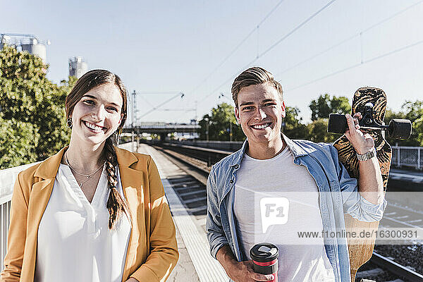 Smiling male and female friends standing at railroad station platform