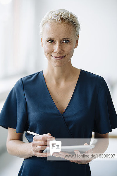 Nahaufnahme einer lächelnden Geschäftsfrau  die ein digitales Tablet benutzt  während sie im Büro steht
