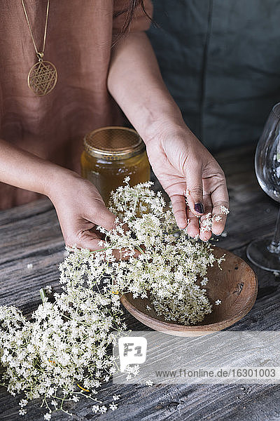Mittelteil einer Frau bei der Zubereitung eines frischen Cocktails mit weißen Blumen auf einem Holztisch