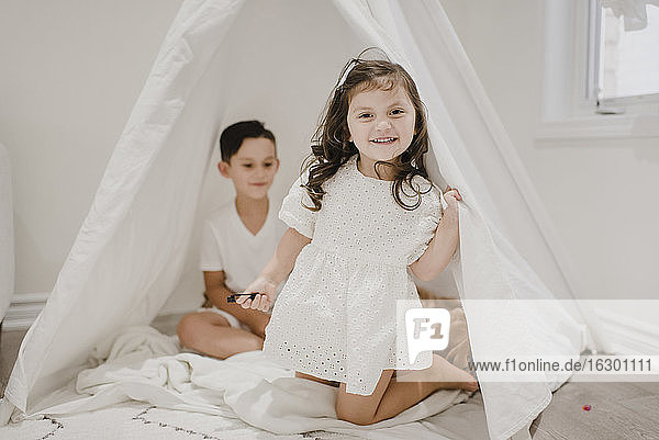 Lächelnde Schwester mit Bruder kniend im Zelt zu Hause