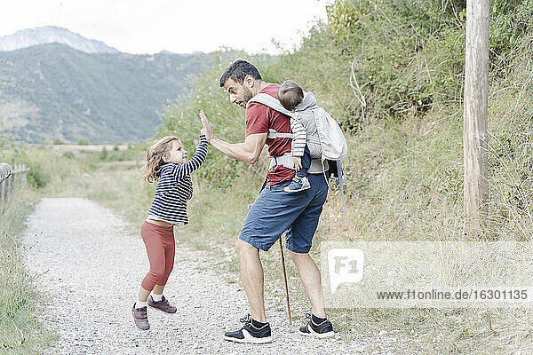 Vater wandert mit seinen Kindern  trägt seinen Sohn auf dem Rücken und gibt seiner Tochter ein High Five
