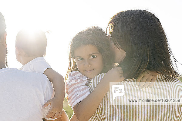 Nettes Mädchen umarmt Mutter von Vater mit Schwester im Park bei Sonnenuntergang