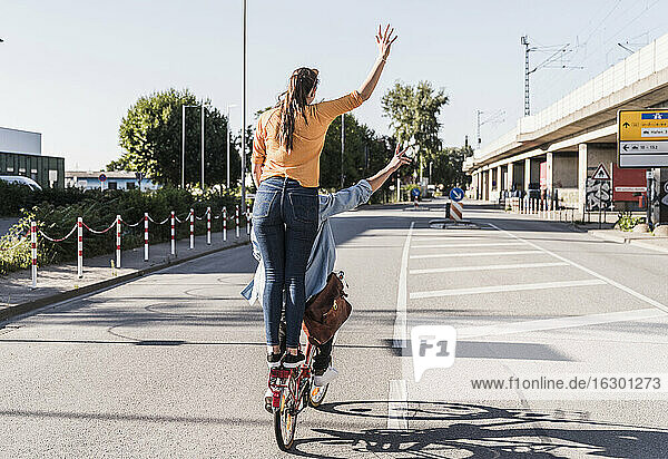 Frau steht hinter ihrem Freund  der auf einer Straße in der Stadt Rad fährt